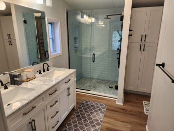 Modern bathroom with double vanity, glass walk-in shower, and wood flooring